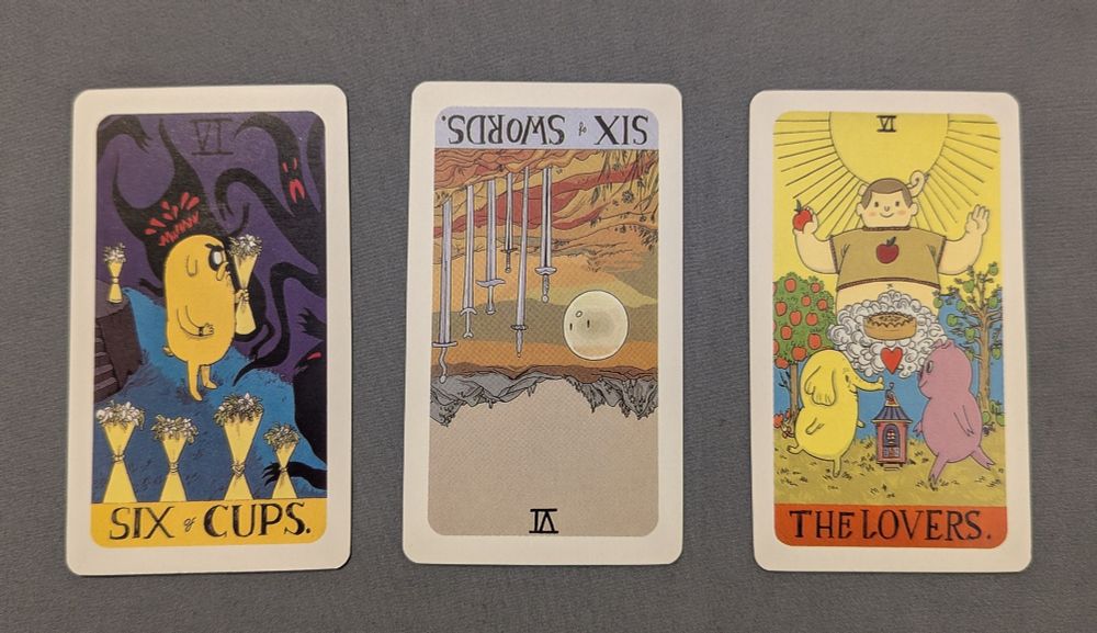 A three-card Tarot spread from Katherine Hillier's "A Totally Unofficial Adventure Time Tarot Deck", showing the Six of Cups, a reversed Six of Swords, and The Lovers