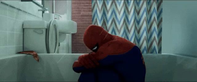 a man in a spiderman costume sits in a bathtub with his head on his knees