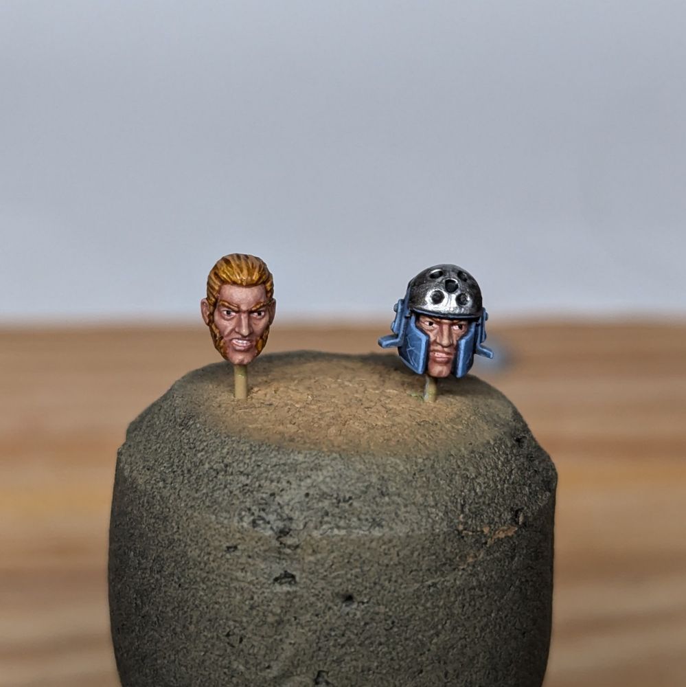Two painted heads for a plastic miniature mounted on a cork. One has a helmet the other has big muttonchop facial hair.