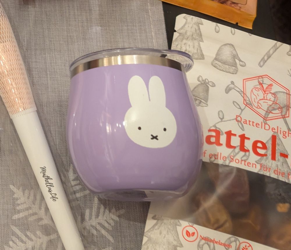 Ein fliederfarbener Trinkbecher mit einem weißen Hasen Motiv.