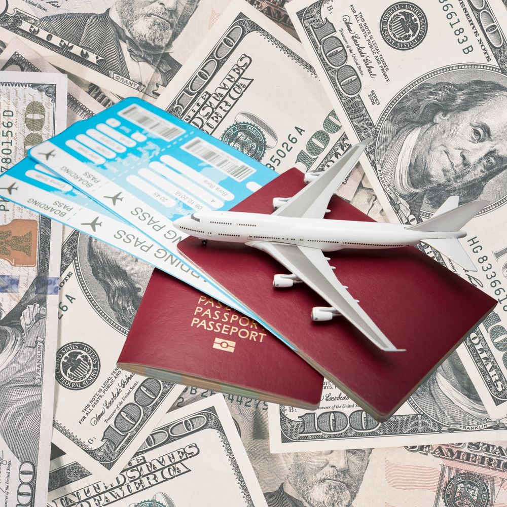 2 red passports and airplane tickets and a toy airplane on top of American money (bills)