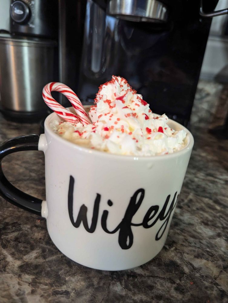 A picture of a late with a candy cane in it, whipped cream, in a wifey mug.