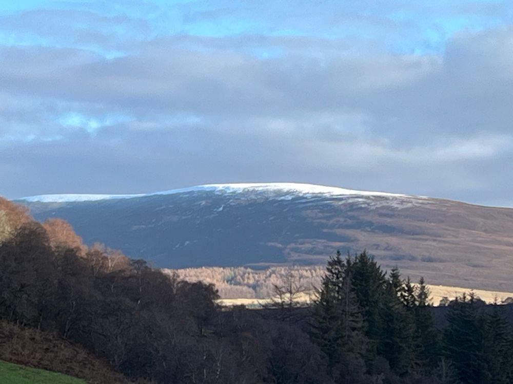 distant hill with the first snow of the season on top. not much yet. clouds and patches of pale blue sky. slanting sun