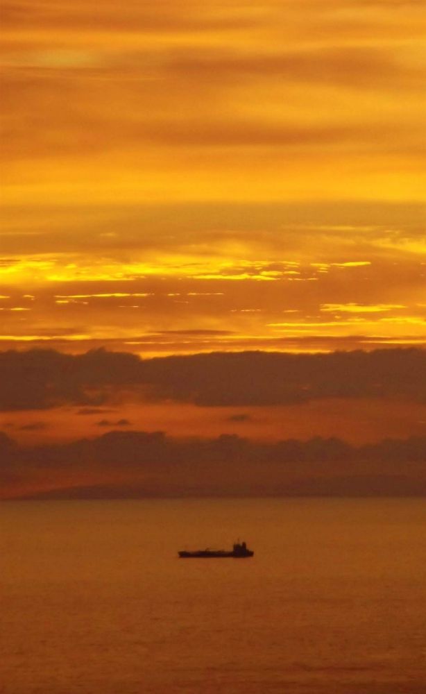 A golden dawn rises over a ship at sea before the distant outline of Fuertaventura. 