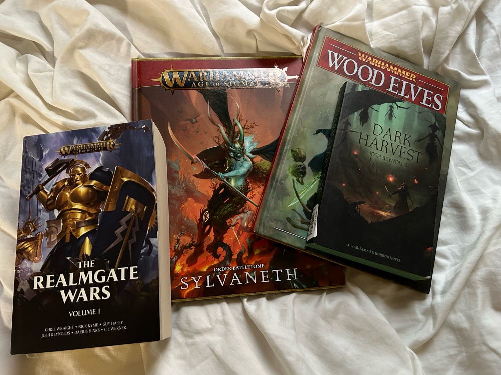 A collection of books relating to Warhammer, including Realmgate Wars Volume 1, army rules for Sylvaneth in Age of Sigmar, army rules for the wood elves in Warhammer Fantasy Battles, and Dark Harvest by Josh Reynolds