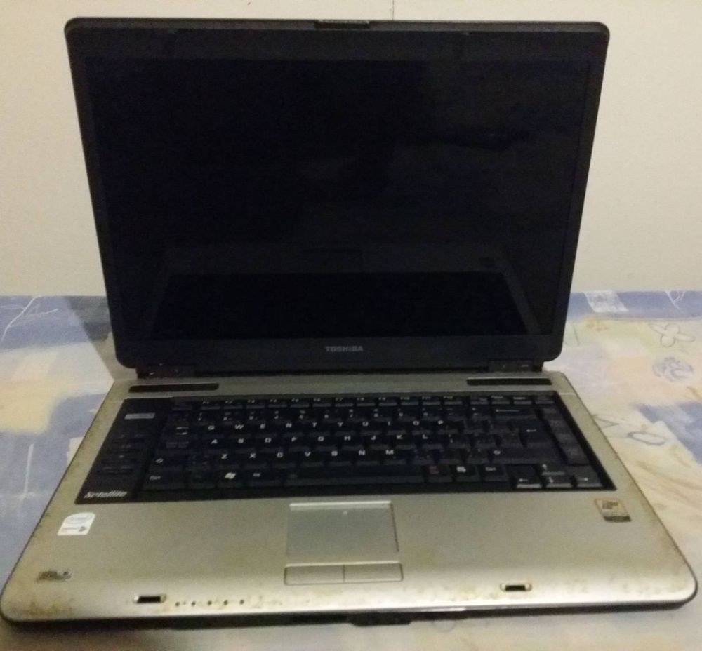 Picture of my Dad's old Toshiba Satellite A100-TA4 Laptop. Its bottom half is silver and has a black keyboard. 