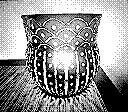 A decorative candle holder with intricate patterns, casting light on a surface. The image is pixelated and in black and white.