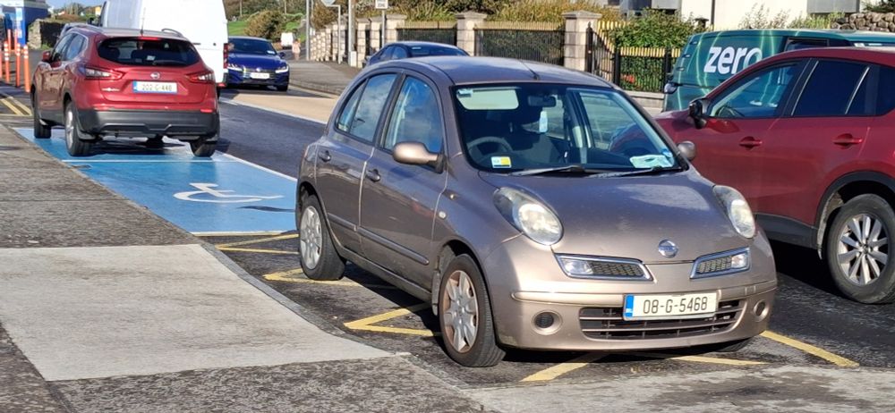 Car parked illegally in a hatched area in front of a Blue Badge space, preventing access to the dished kerb.