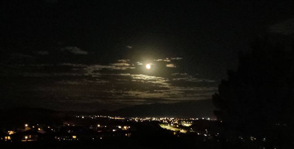 Moon with clouds and the lights of a city below 