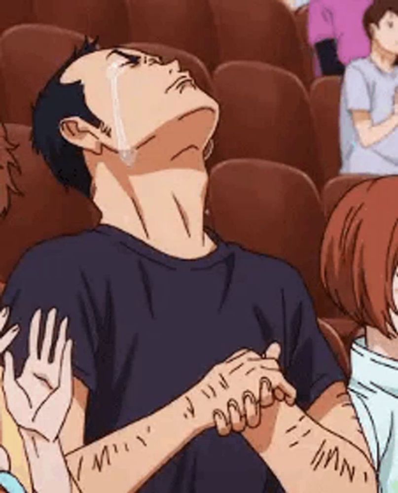 a man in a black shirt is crying while sitting in a theatre .