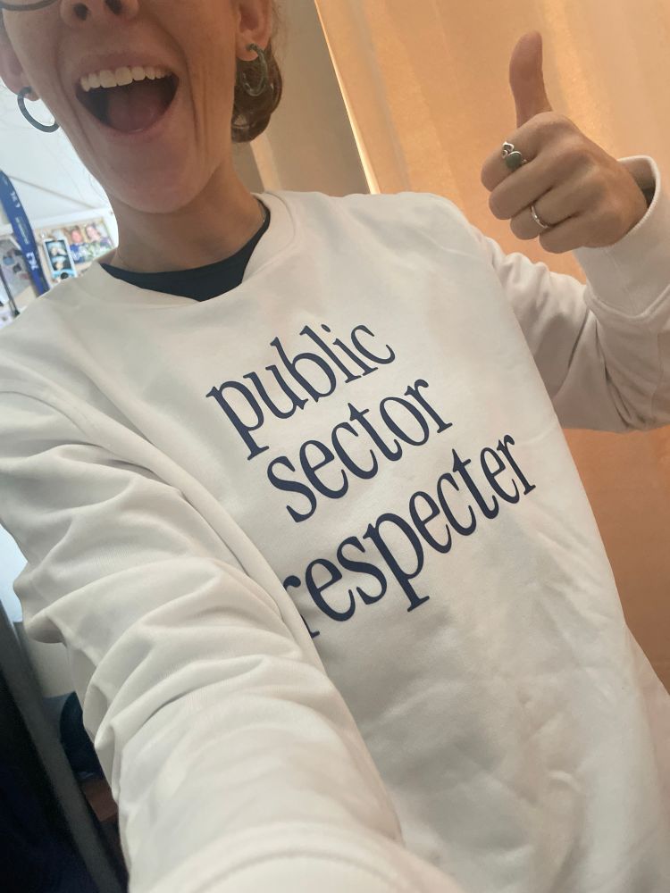 Wearing a white crew neck sweater that says “public sector respecter”