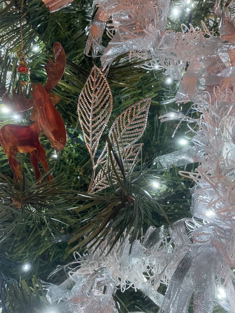 A close up picture of a Christmas tree with white lights, white garland, a trio of silver leafs, and a coppery moose ornament. 