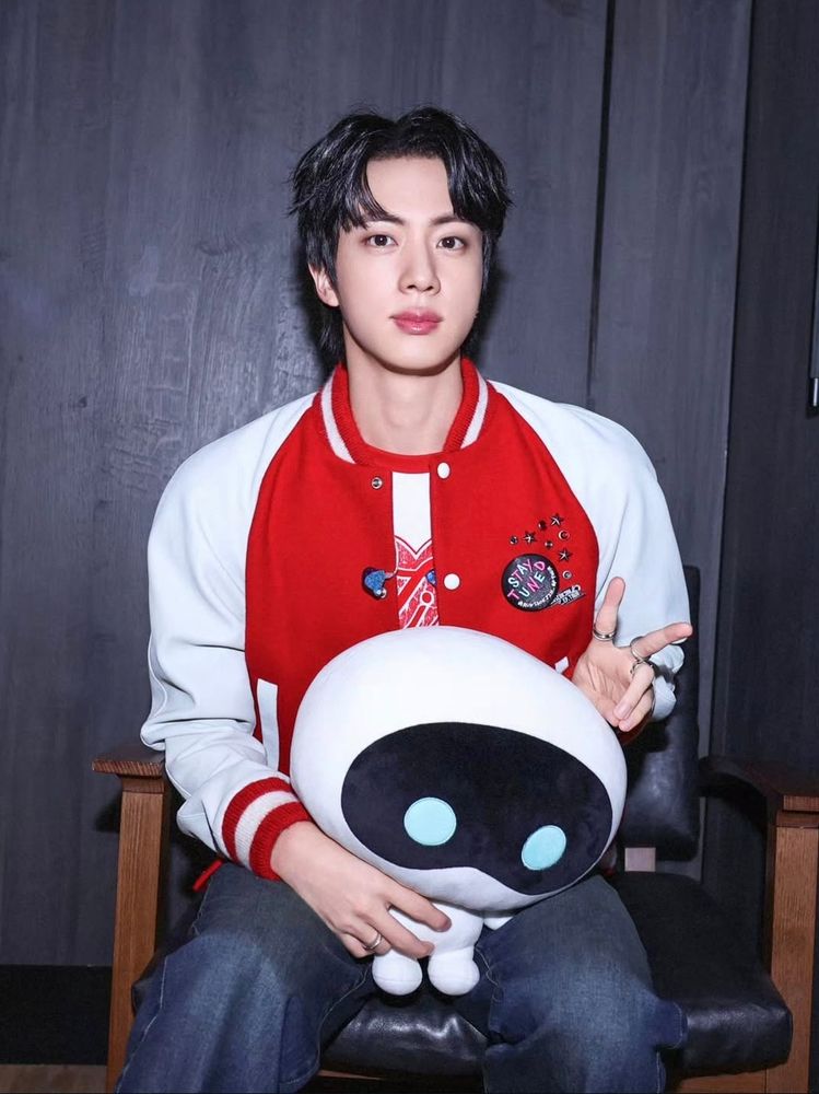 Jin sports a red letterman jacket and gives a peace sign while Wootteo enjoys lap privilege.