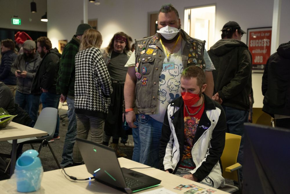 Two gamers playing a game on a laptop with a crowd in the background