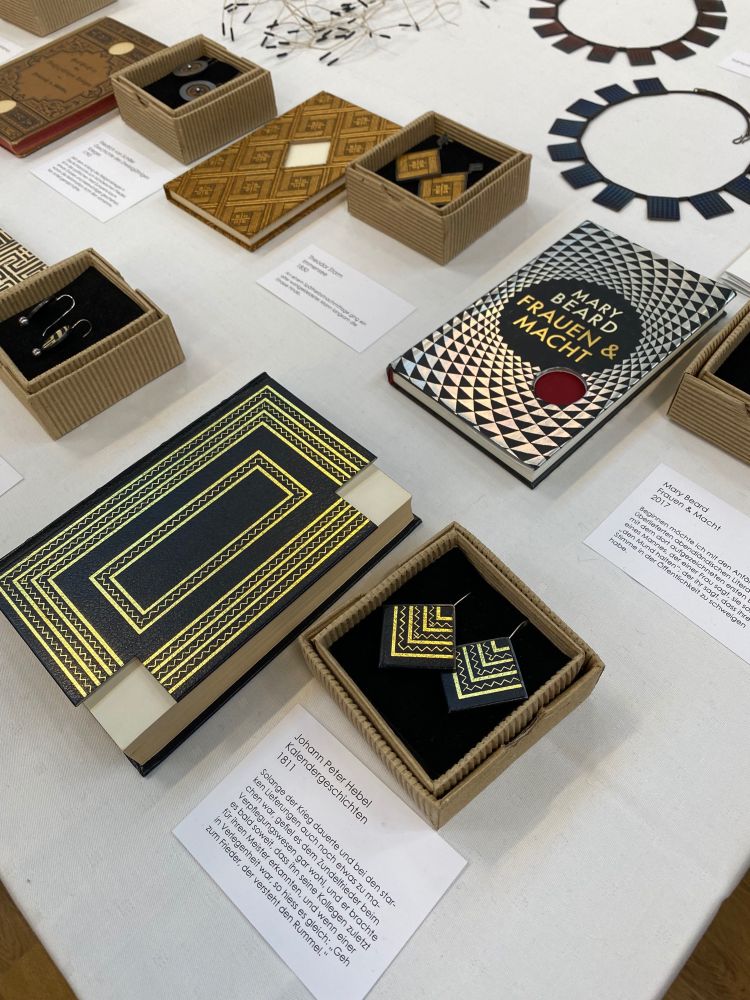 Ein Messestand mit Schmuckstücken aus Büchern. In kleinen Schachteln liegen je zwei Ohrringe, gestaltet aus Teilen von Buchdeckeln. 