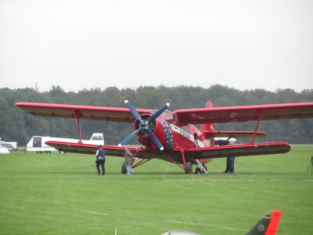 Ein roter Doppeldecker steht auf dem Flugfeld. Davor gehen zwei Leute. 