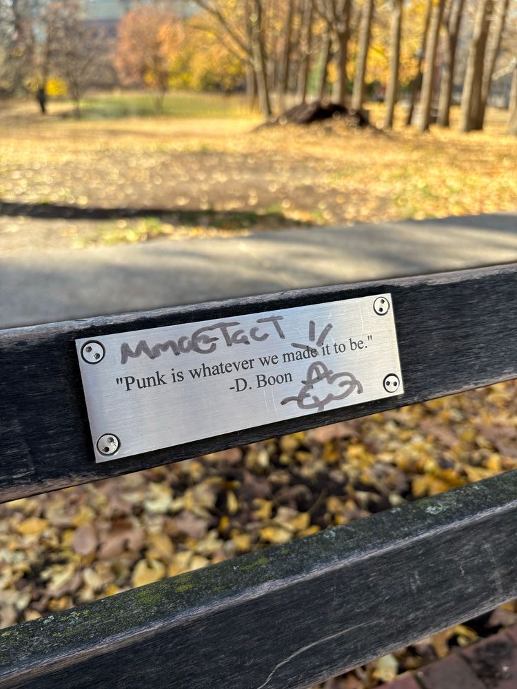 A bench plaque with the quote “Punk is whatever we made it to be,” from D. Boon of the Minutemen. Someone drew a penis with cum coming out of it on the plaque. 