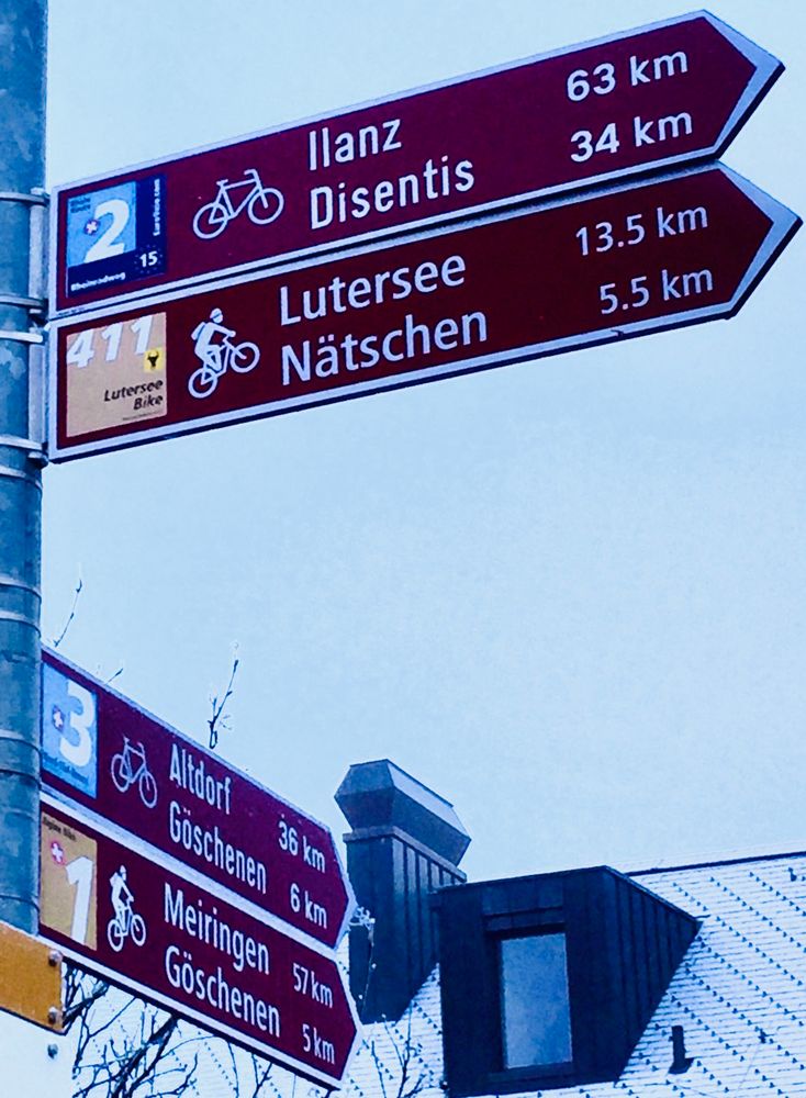 Ein Wegweiser für Fahrrad- und Mountainbike-Strecken; im Hintergrund ein schneebedecktes Dach