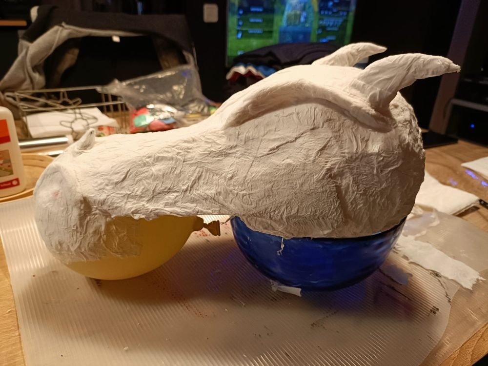 A homemade dragon-like mask (still a work in process) made of maché paper on top of a bowl and tied to a balloon.
