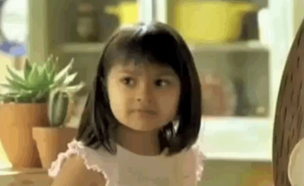 a little girl is making a funny face while sitting at a table with potted plants .