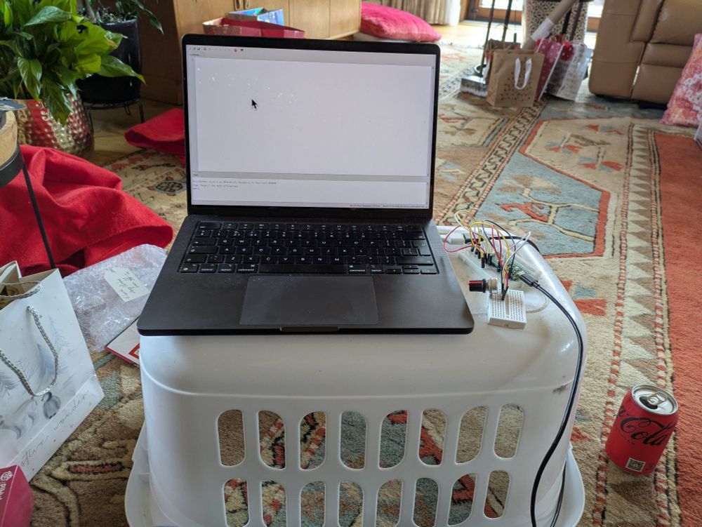 A laptop with breadboard plugged in on top of a upside-down washing basket. 