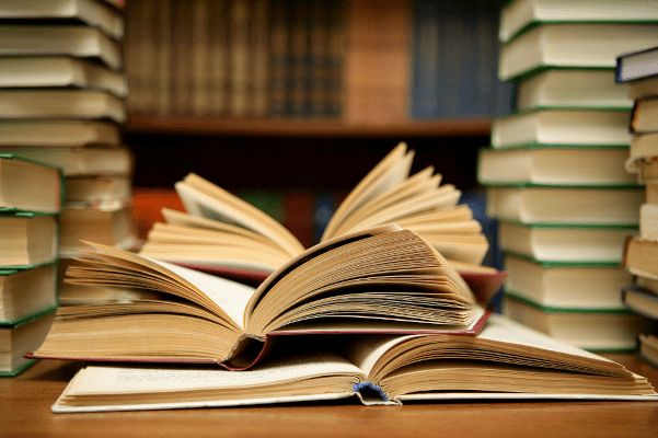 Ein Tisch, auf dem sich Bücher am Rand stapeln. In der Mitte befinden sich aufgeschlagene Bücher. ("Books HD" by Abee5 is licensed under CC BY 2.0.)