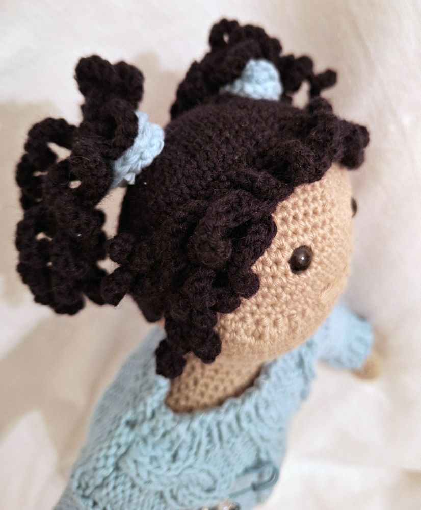 Detailaufnahme von Oktavias Kopf mit den lockigen schwarzen Zöpfen. Außerdem hat sie einen kleinen lockigen Pony, der das Gesicht umrahmt.  