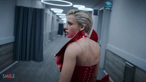 a woman in a red dress is walking down a hallway with the word smile on the bottom right