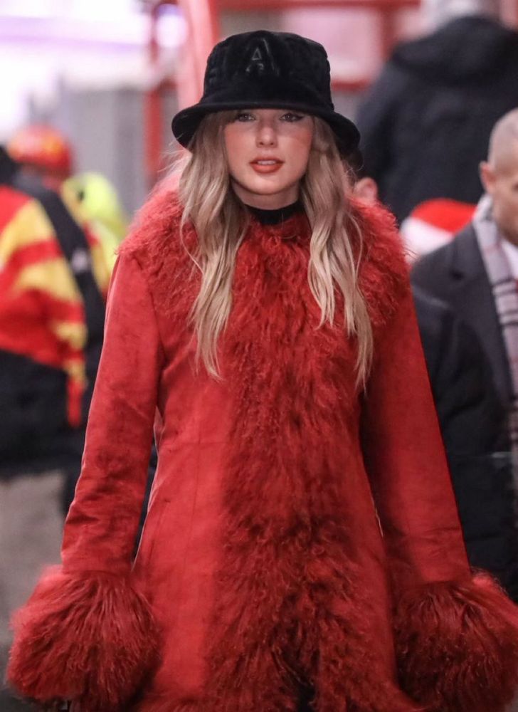 Taylor Swift wearing a black hat and red coat with fluffy red trim 