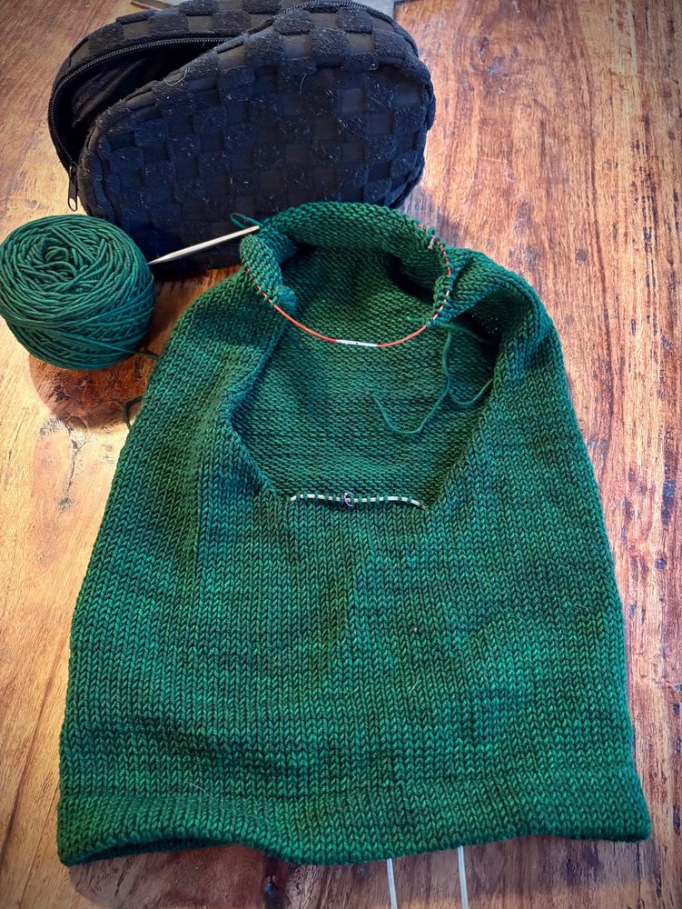 A Hand-dyed green knitted hood lays on a wooden table. 