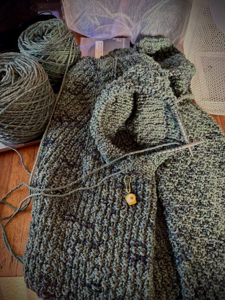 Green and speckled blue handspun yarn being knit into a Gib sweater by Drea Renee Knits aka Andrea Mowry. Sleeves are being picked up and knit with alternating balls of yarn.