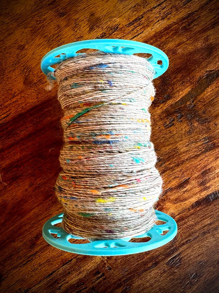 A bobbin is 3/4 full of grey, rainbow tweed wool singles.