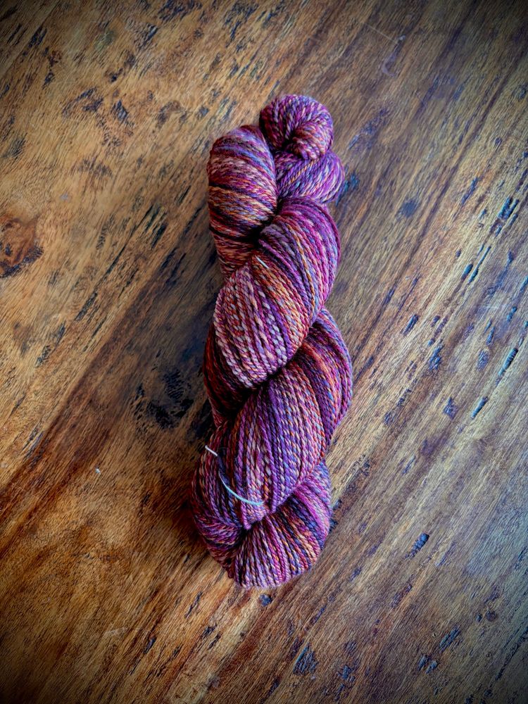A finished skein of handspun yarn. The colors are marled with tones of purple, orange and burgundy. 
