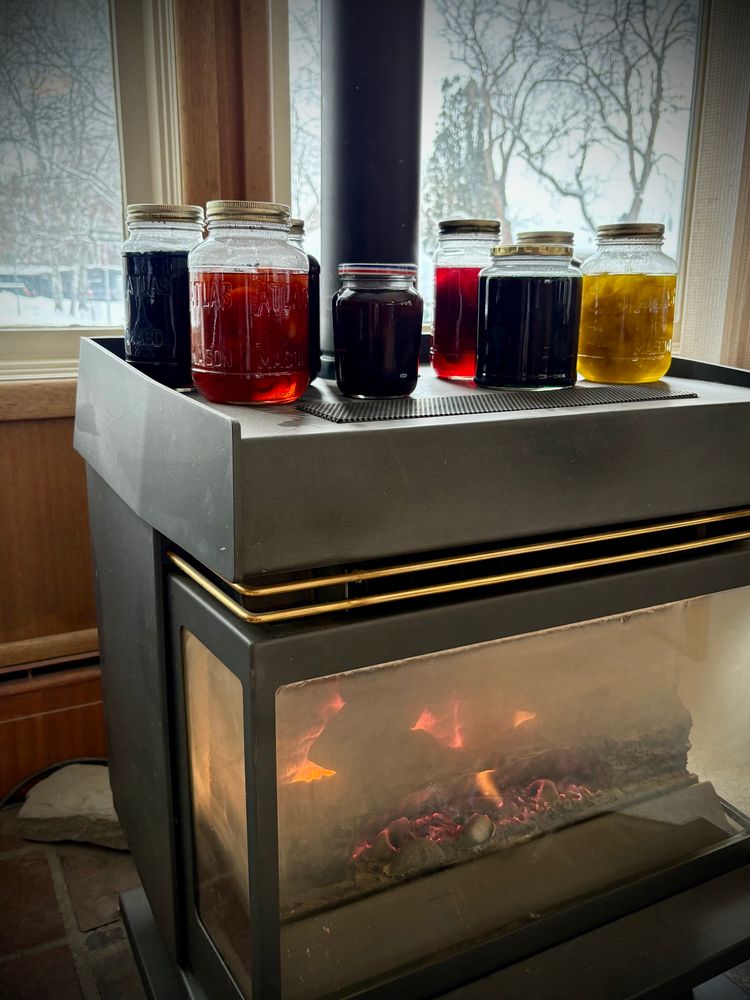 Eight jars filled with a rainbow of dye and sari silk sit atop a lit gas stove. 
