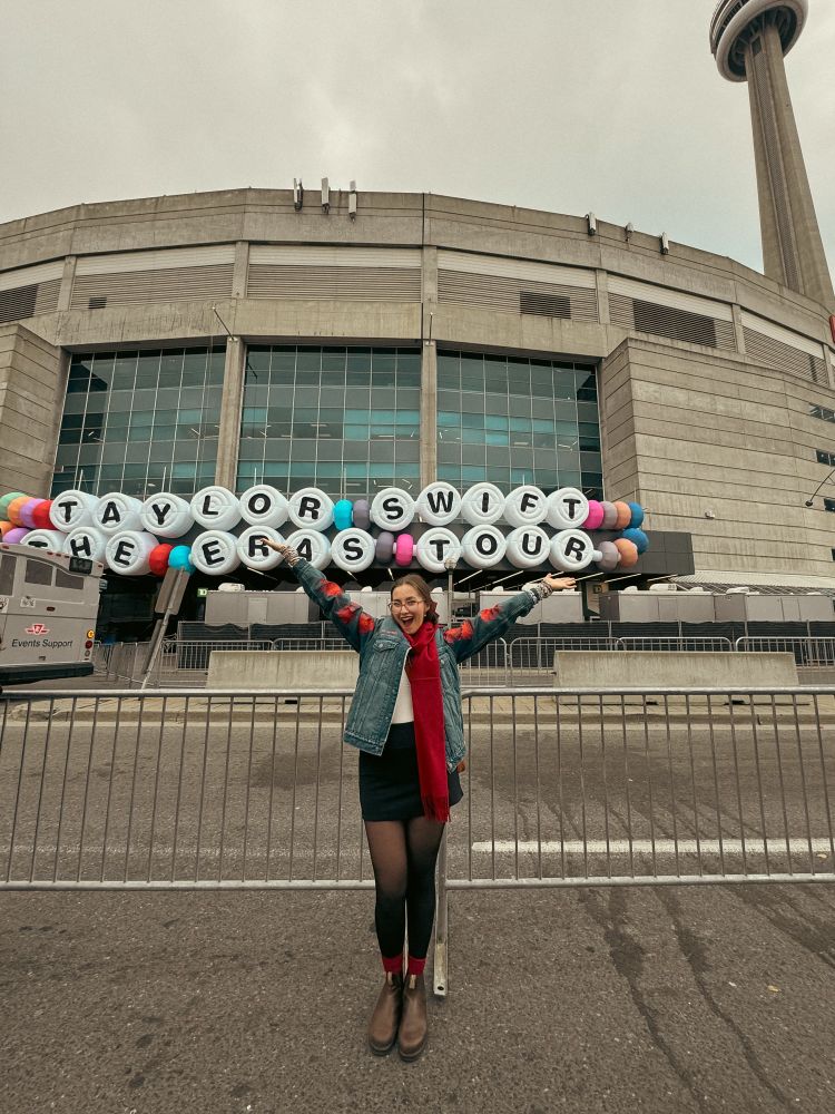Laurence wearing a Jean jacket and red scarf in front of the inflatable friendship bracelet in Roger Center 