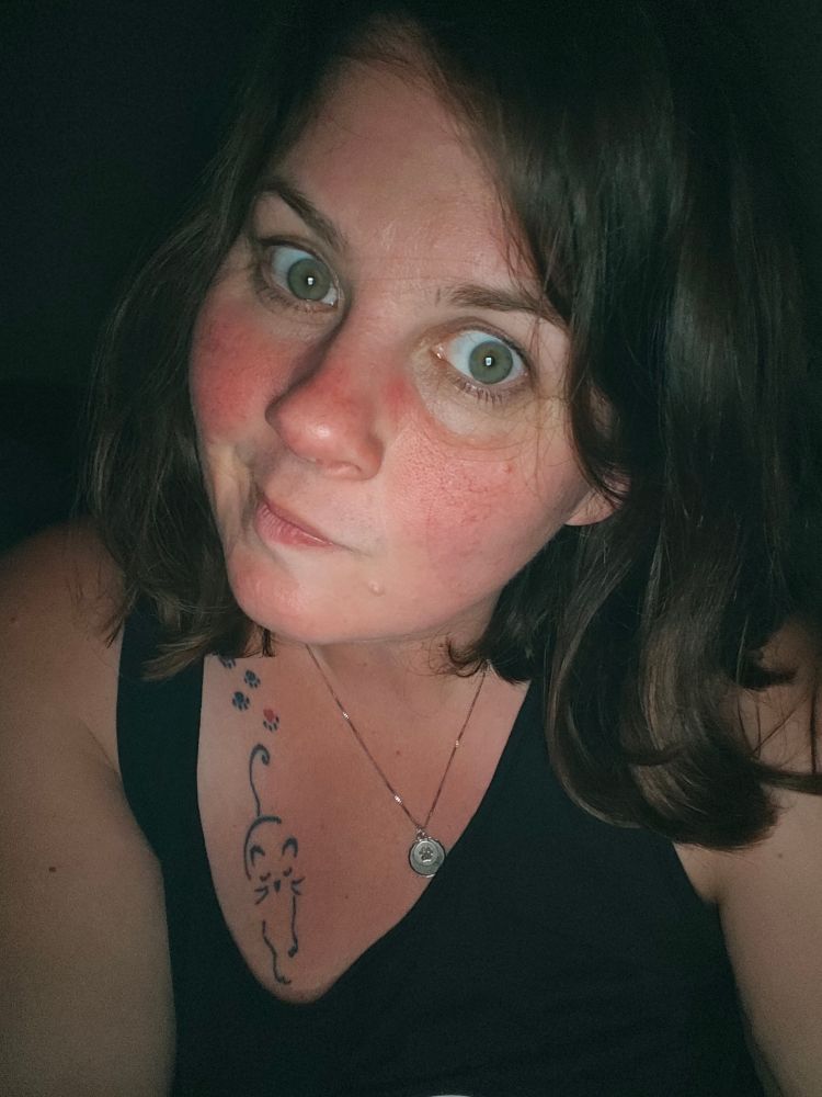 Ein Foto von mir, ziemlich müde und erschöpft. 
Braune schulterlange Haare, grüne Augen, den Mund leicht verzogen. 
Ein Tattoo ist im Dekolleté zu sehen, eine Katze und ihre Spuren.