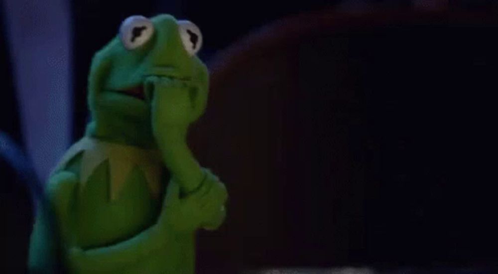 kermit the frog is covering his mouth with his hand and looking at the camera .