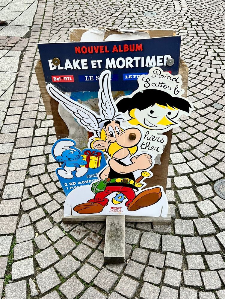 A sign for a French comic shop that features overlapping cutouts for Asterix, the Smurfs, Blake et Mortimer, and other Franco-Belgian comics