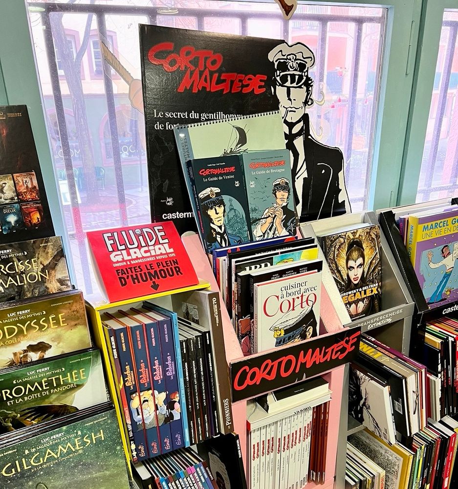 Interior of the comic shop featuring many comics albums, including various books from Fluide Glacial and a display of Corto Maltese books