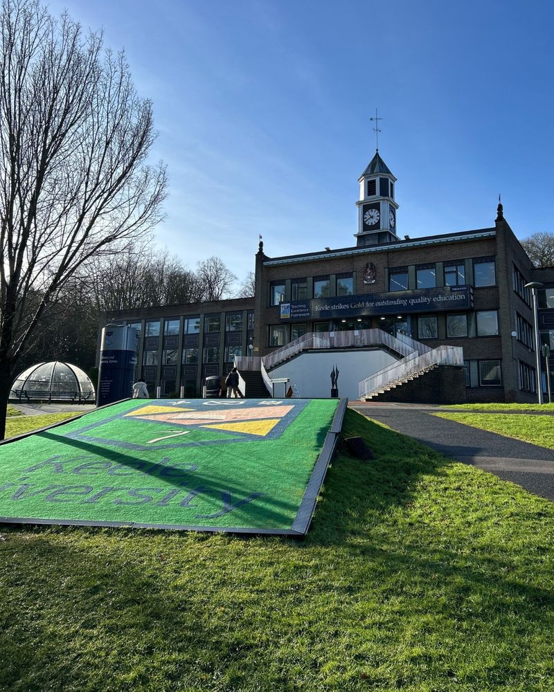 A view of the campus library with the Keele University logo prominently displayed on the floor. The sky is clear and blue