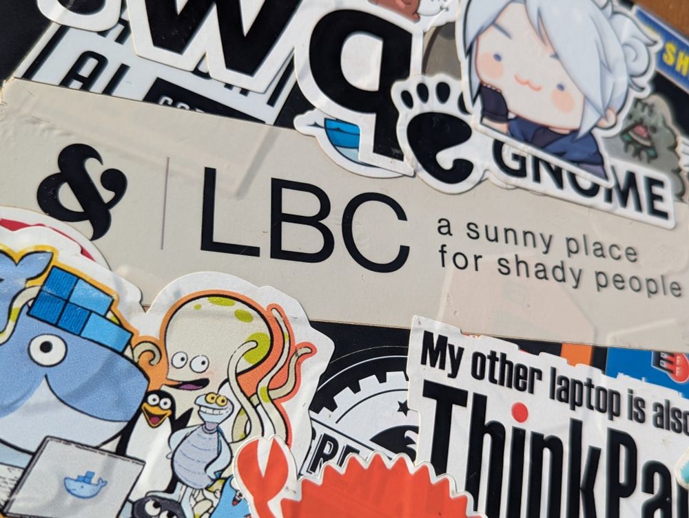 A laptop sticker saying "LBC a sunny place for shady people" overlapping many others