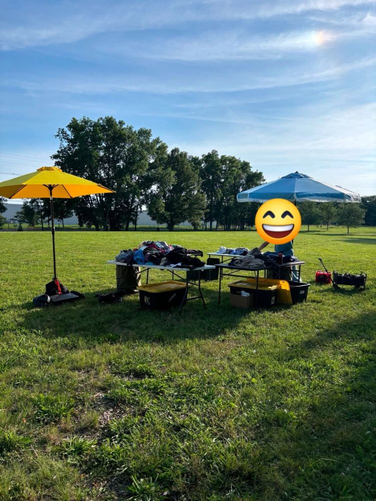 Image shows two tall umbrellas, one that is yellow and one that is blue. 
There is green grass and trees in the background. 
We live and serve on stolen and occupied indigenous land. 
