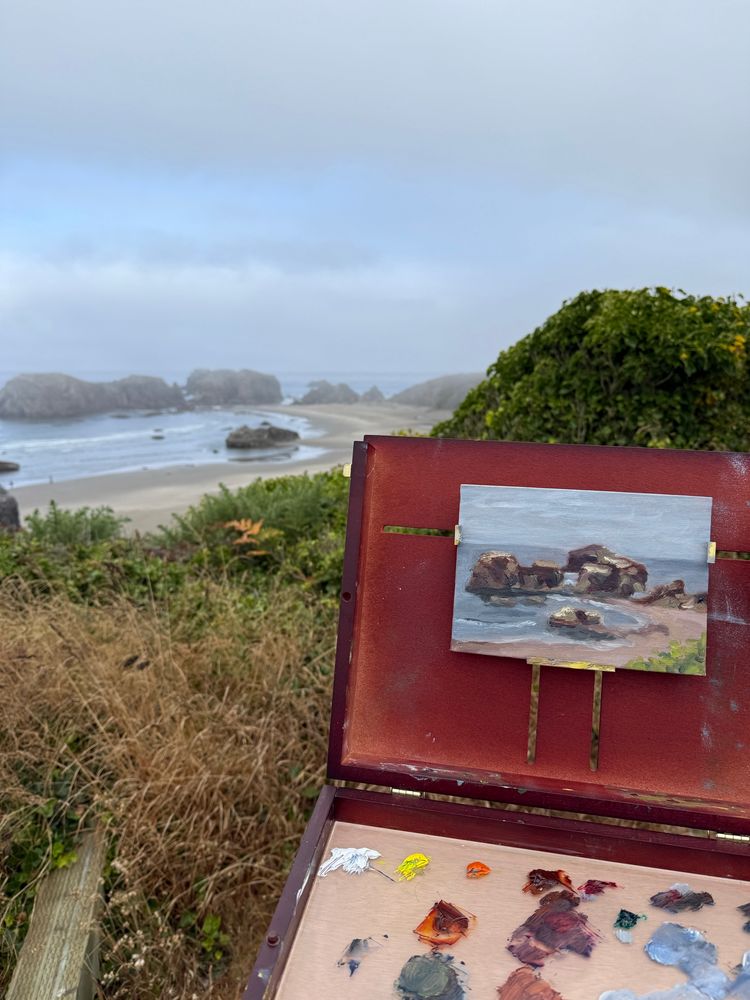 A plein air pinging set up with pochade box overlooking the Oregon coast with sea stacks, tide pools, and ocean in the distance