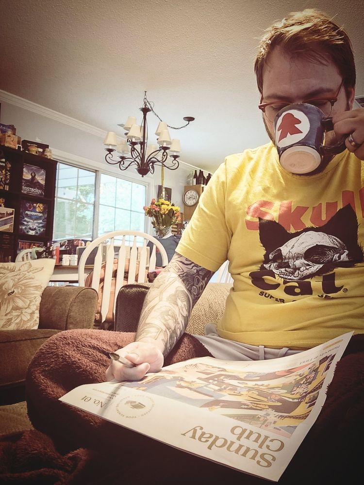 Luke drinking coffee, admiring the front page of the Sunday Club paper