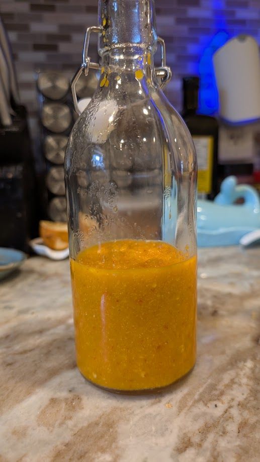 A swing-top bottle about a third-full of an orange hot sauce.