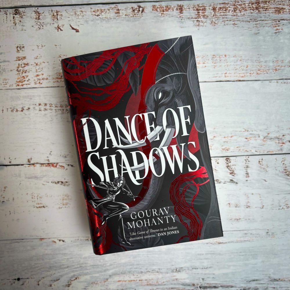 A book titled "Dance of Shadows" by Gourav Mohanty, featuring a vivid red and black cover design with intricate patterns and a central figure engaged in a fighting stance.