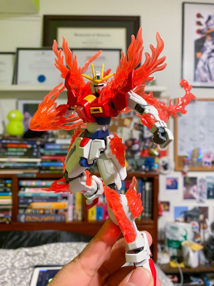 A hand holding a fully built Try Burning Gundam. It looks like it’s ready to punch someone. It’s right hand is behind it getting ready to punch someone with flames