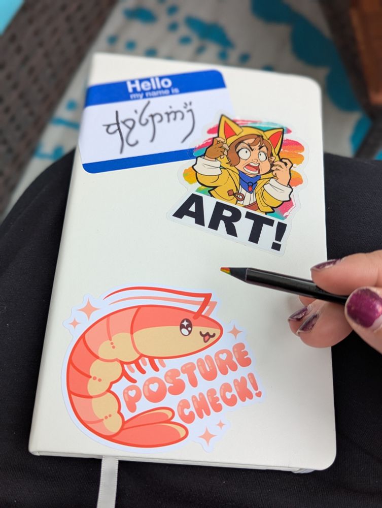 A white sketchbook with 3 stickers - a name in elvish from Lord of the Rings, Krile from FFXIV screaming art, and a cute shrimp saying posture check. Also a hand holding a black rainbow pencil.