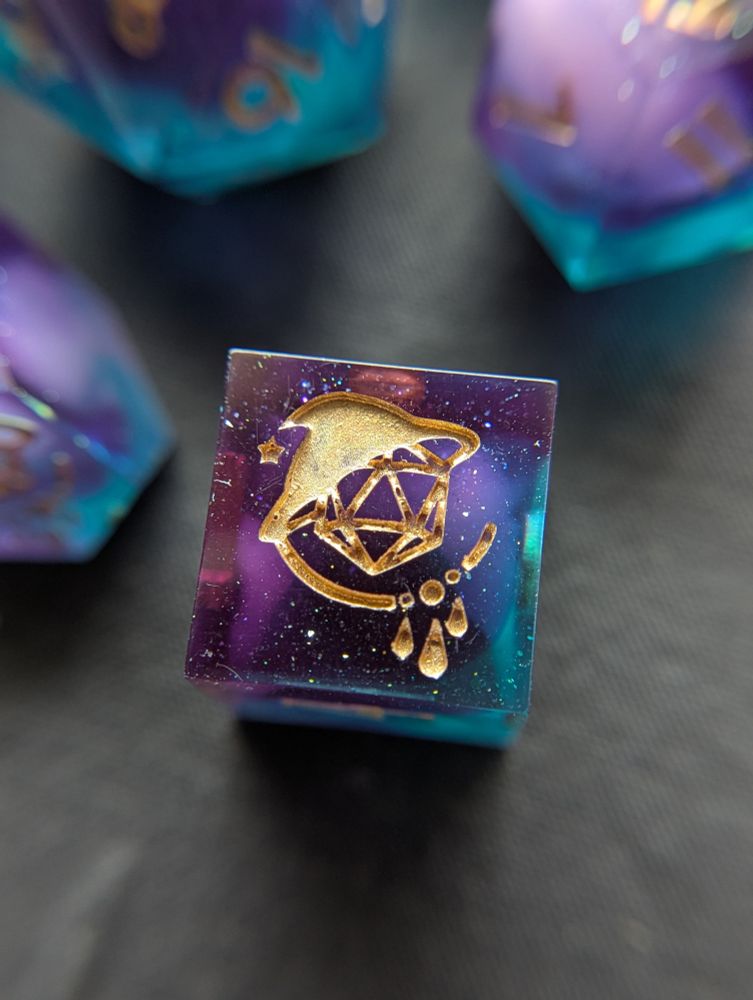 Handmade dice with white swirls in purple and teal transparent resin. They are inked gold.