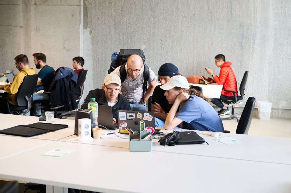 Johannes Schicking, Nik Graf, Leo Stewen, and myself huddled around a laptop with stickers on it. More people in the background